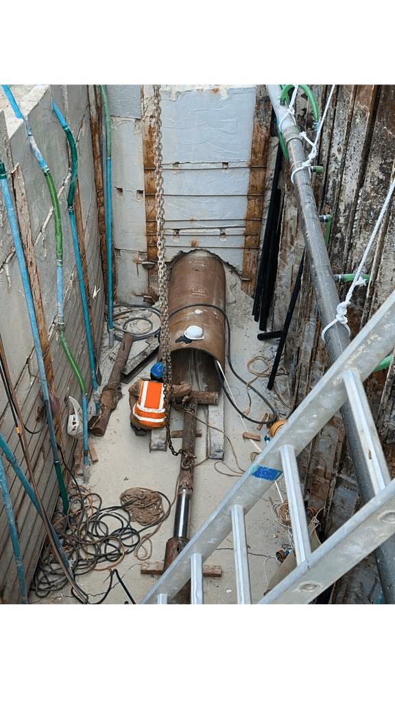 Underground construction site with metal pipes, cables, and a safety vest on the ground.